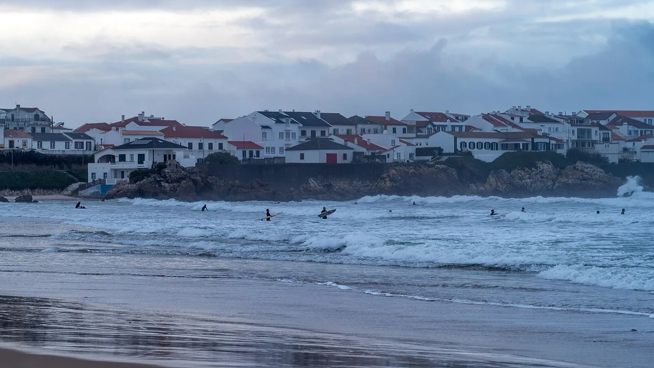 Surfeurs dans l'eau devant les maisons blanches de Baleal, à Peniche