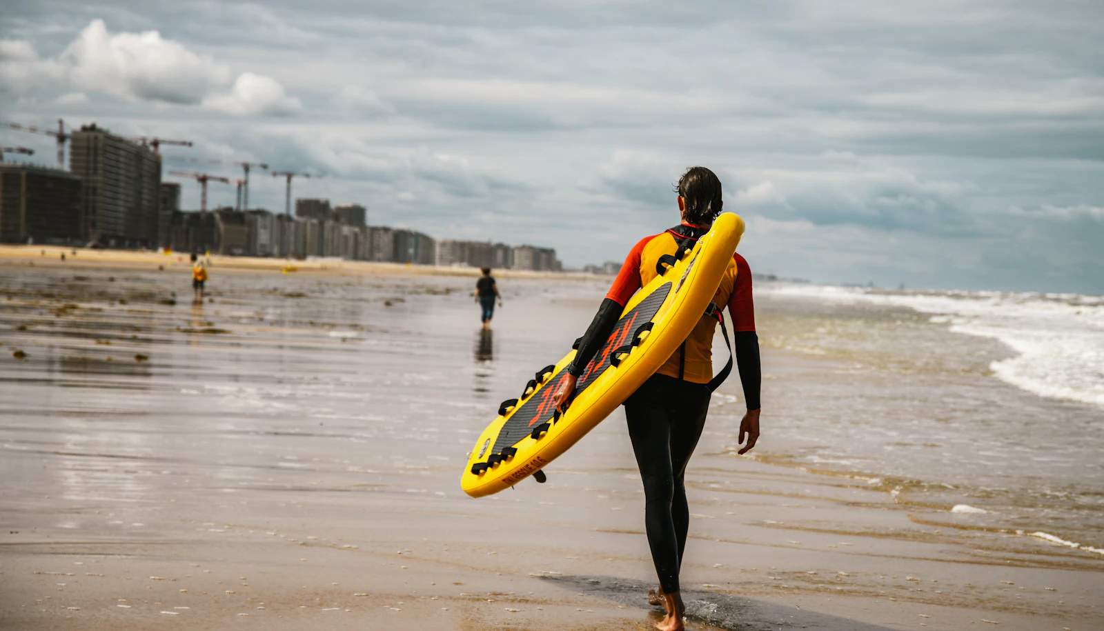 Surfeur portant sa planche sur la plage d'Ostende, côte belge de la mer du Nord