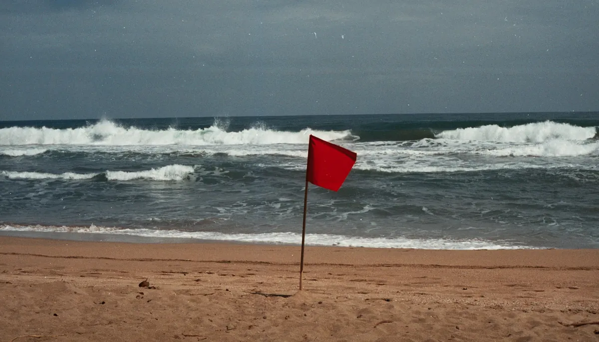 Drapeau rouge planté dans le sable d'une plage, vagues déferlantes derrière