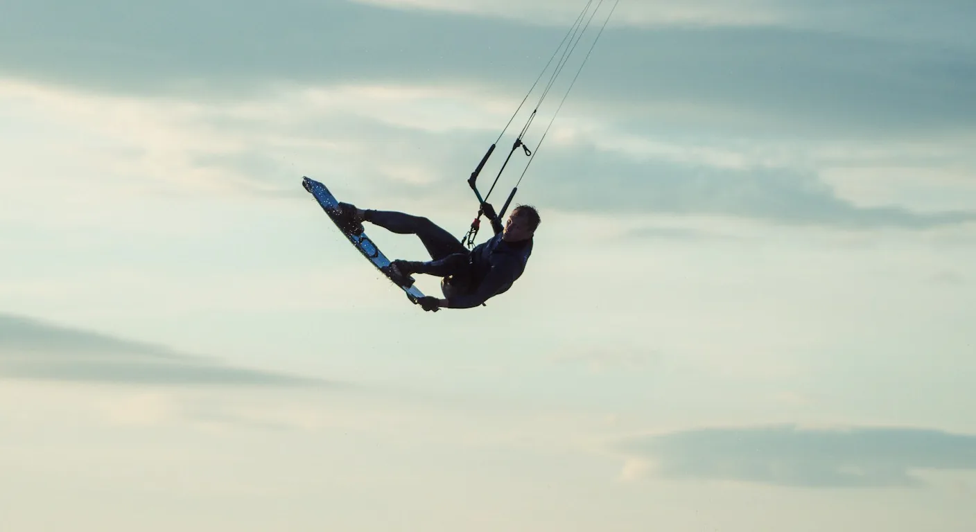 Kitesurfeur en plein saut, suspendu à sa barre sous un ciel nuageux