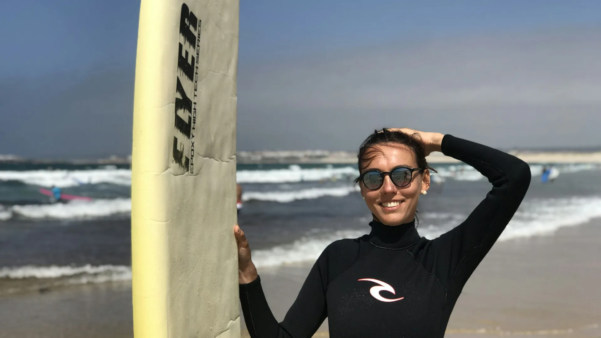 Surfeuse portant une combinaison néoprène noire sur une plage, planche à la main