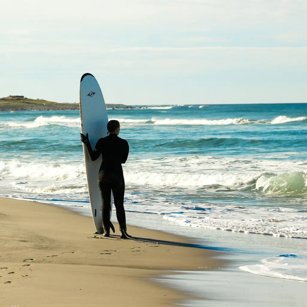 Surfeur homme portant une combinaison néoprène noire sur une plage atlantique