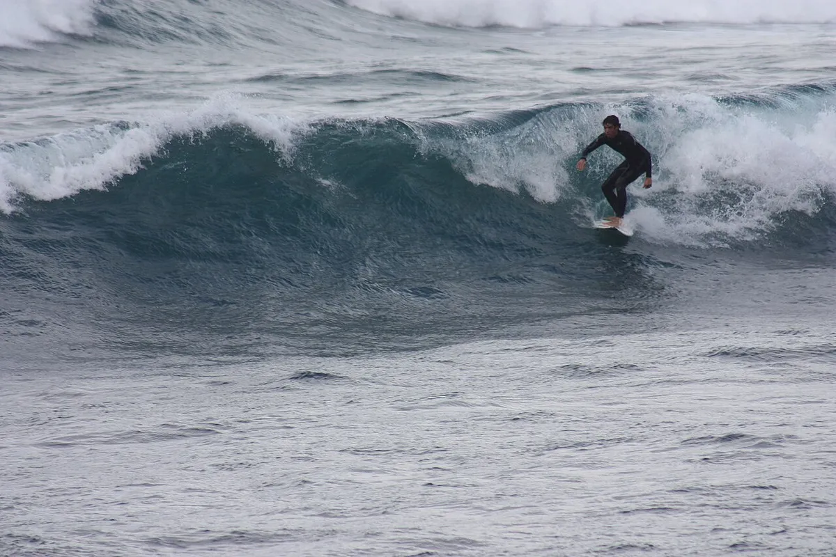 Surfeur en combinaison noire sur la face d'une vague qui déferle, à Caleta de Famara