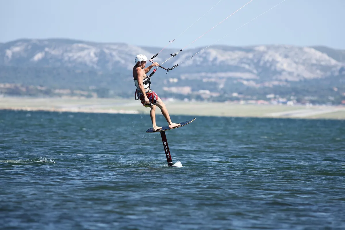 Pratiquant de kite foil coiffé d'un casque blanc et équipé d'un harnais, en vol au-dessus de l'eau