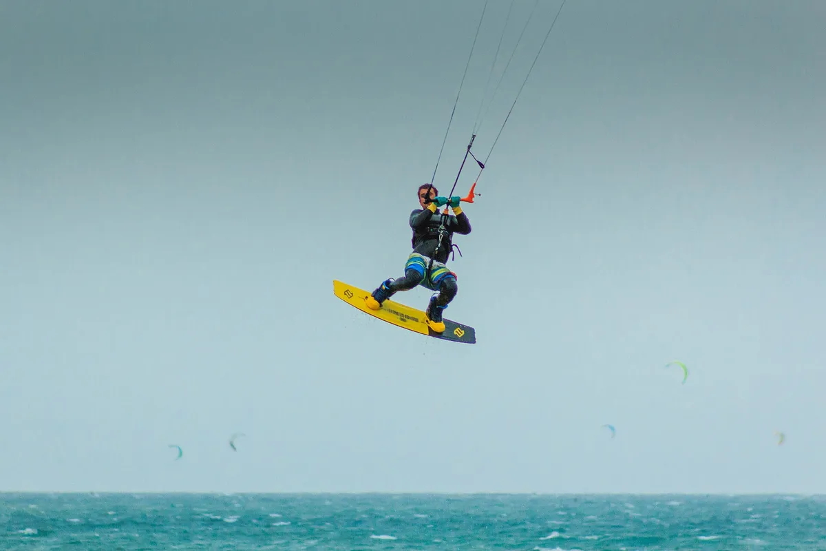 Kitesurfeur en plein saut au-dessus de la mer, planche aux pieds et lignes tendues vers l'aile
