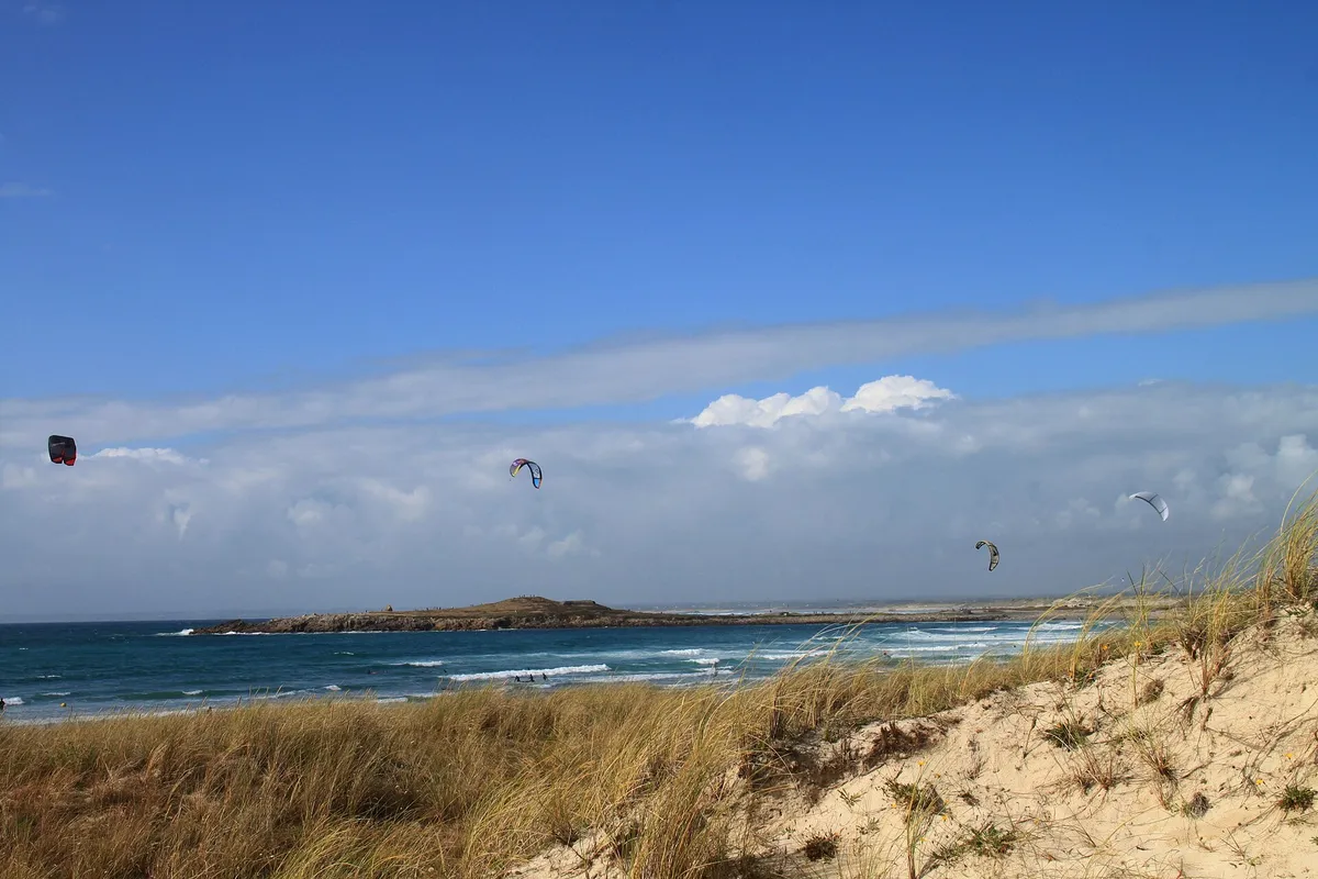 Ailes de kitesurf dans le ciel au-dessus de la plage de la pointe de la Torche, avec des dunes herbeuses au premier plan