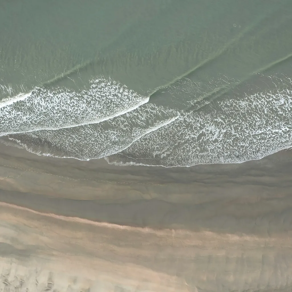 Plage de sable mouillé où viennent mourir de petites vagues, vue du ciel