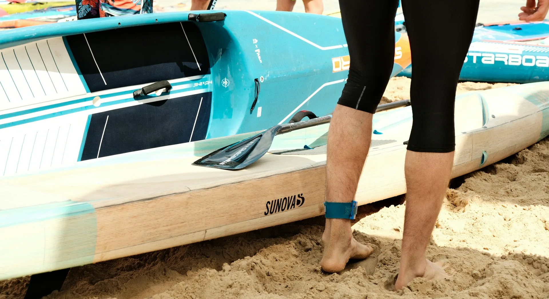 Pagaie et leash posés sur des planches de paddle, sur le sable