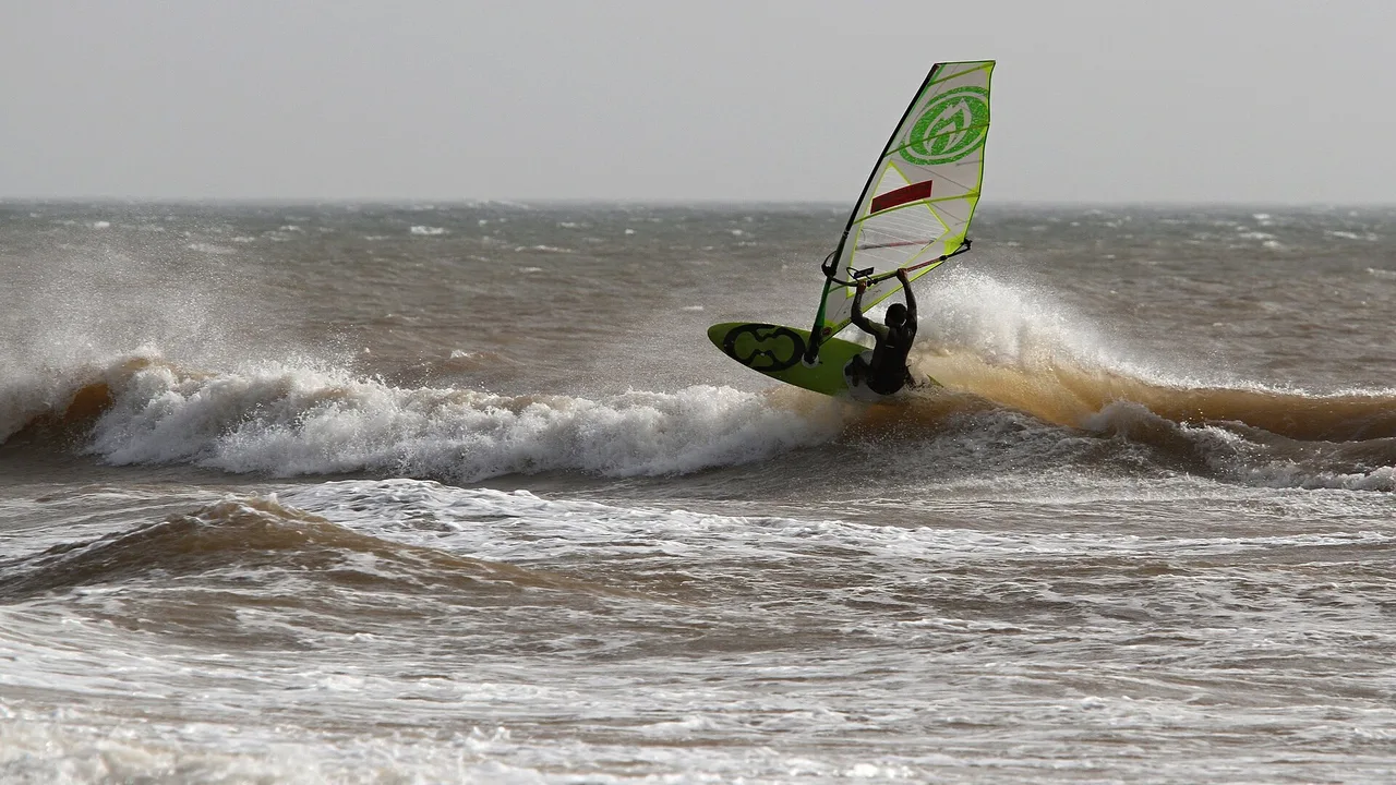 Véliplanchiste sur une vague, voile verte et blanche, à Moulay Bouzerktoun