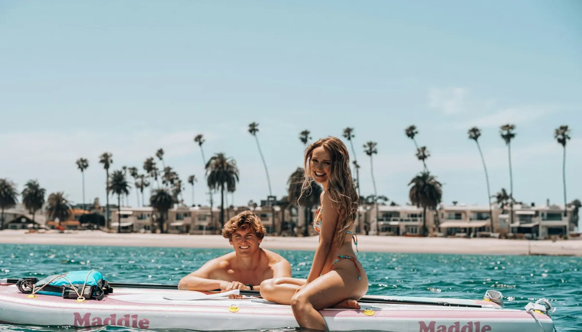Couple assis ensemble sur un grand paddle, près d'une plage bordée de palmiers