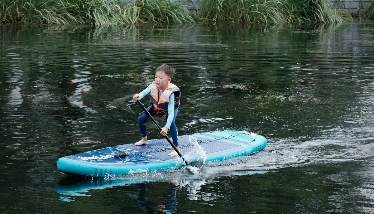 Enfant debout seul sur une planche de paddle, gilet de sauvetage sur le dos