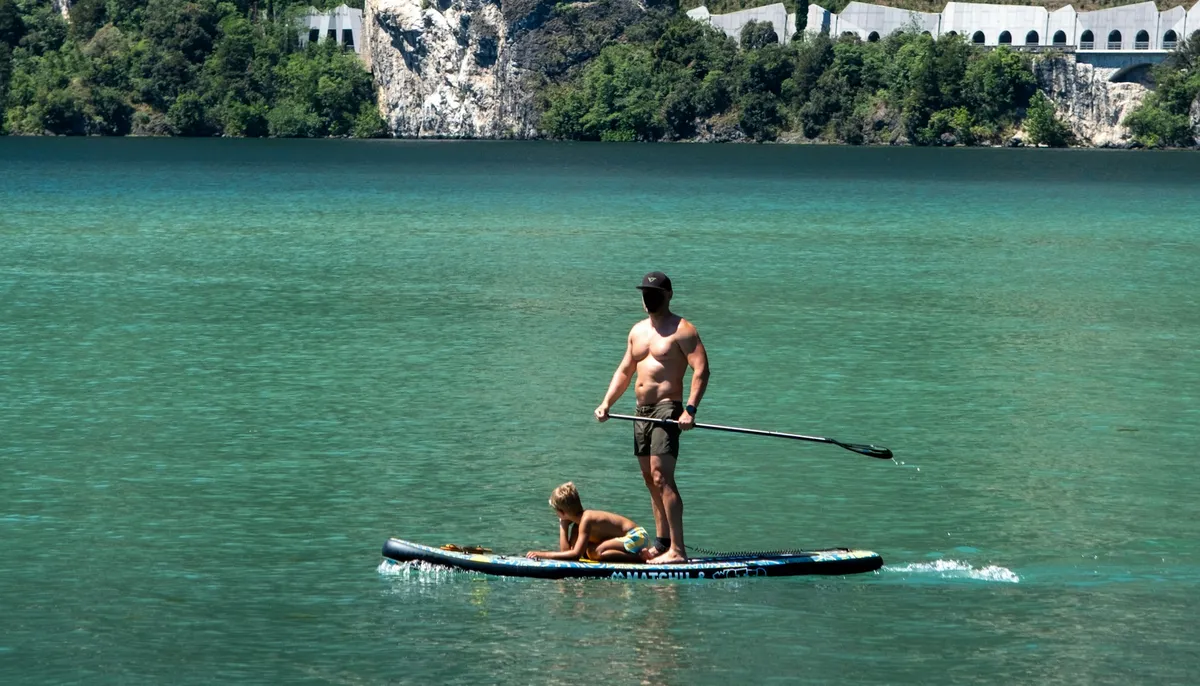 Un adulte debout avec sa pagaie et un enfant assis sur le même paddle, sur un lac aux eaux turquoise