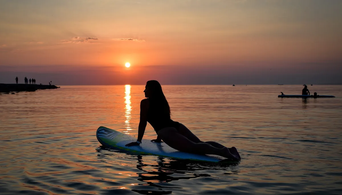 Pratiquants de SUP fitness et yoga sur planche au coucher de soleil