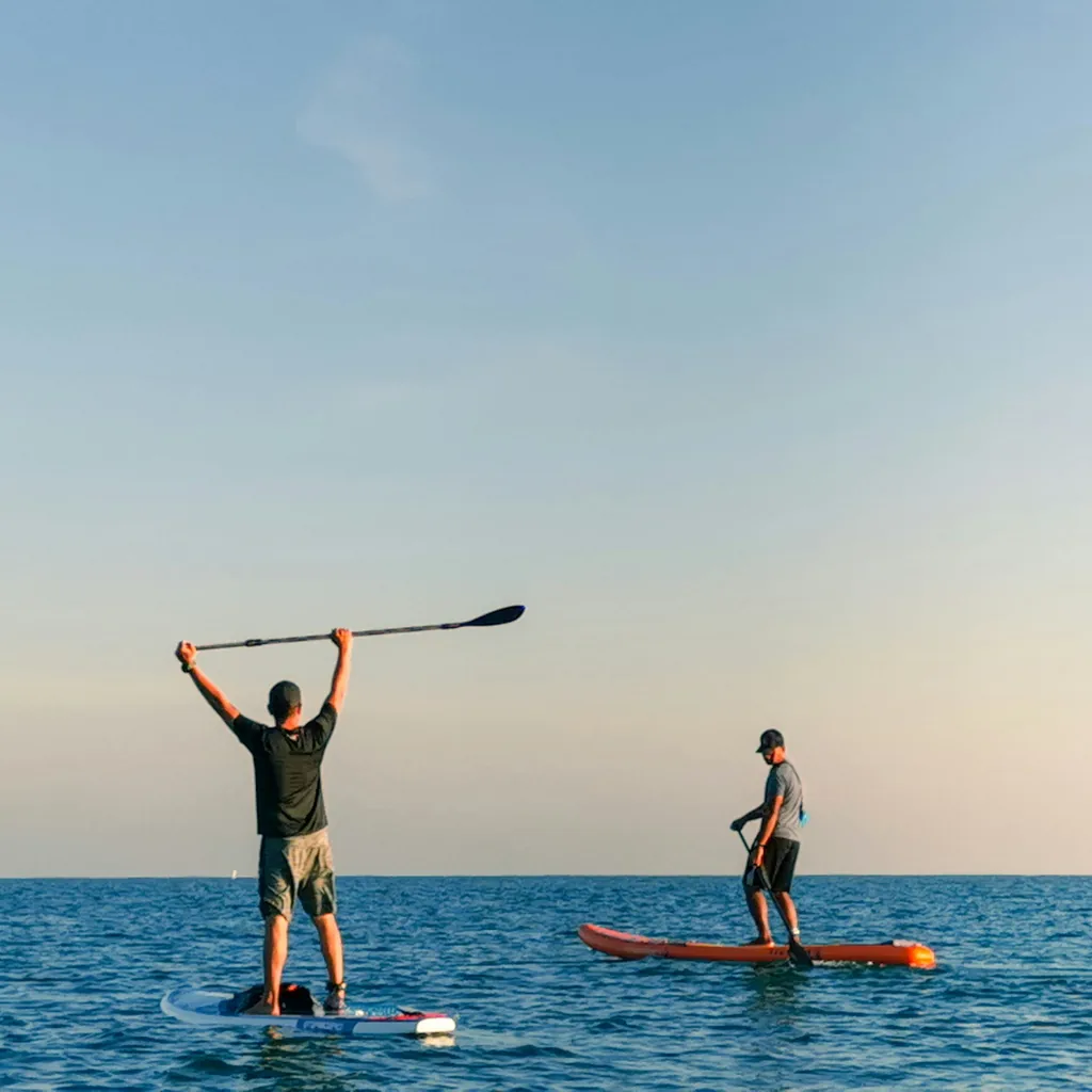 Deux paddleurs debout sur leurs planches sur une eau calme, l'un bras levés avec sa pagaie