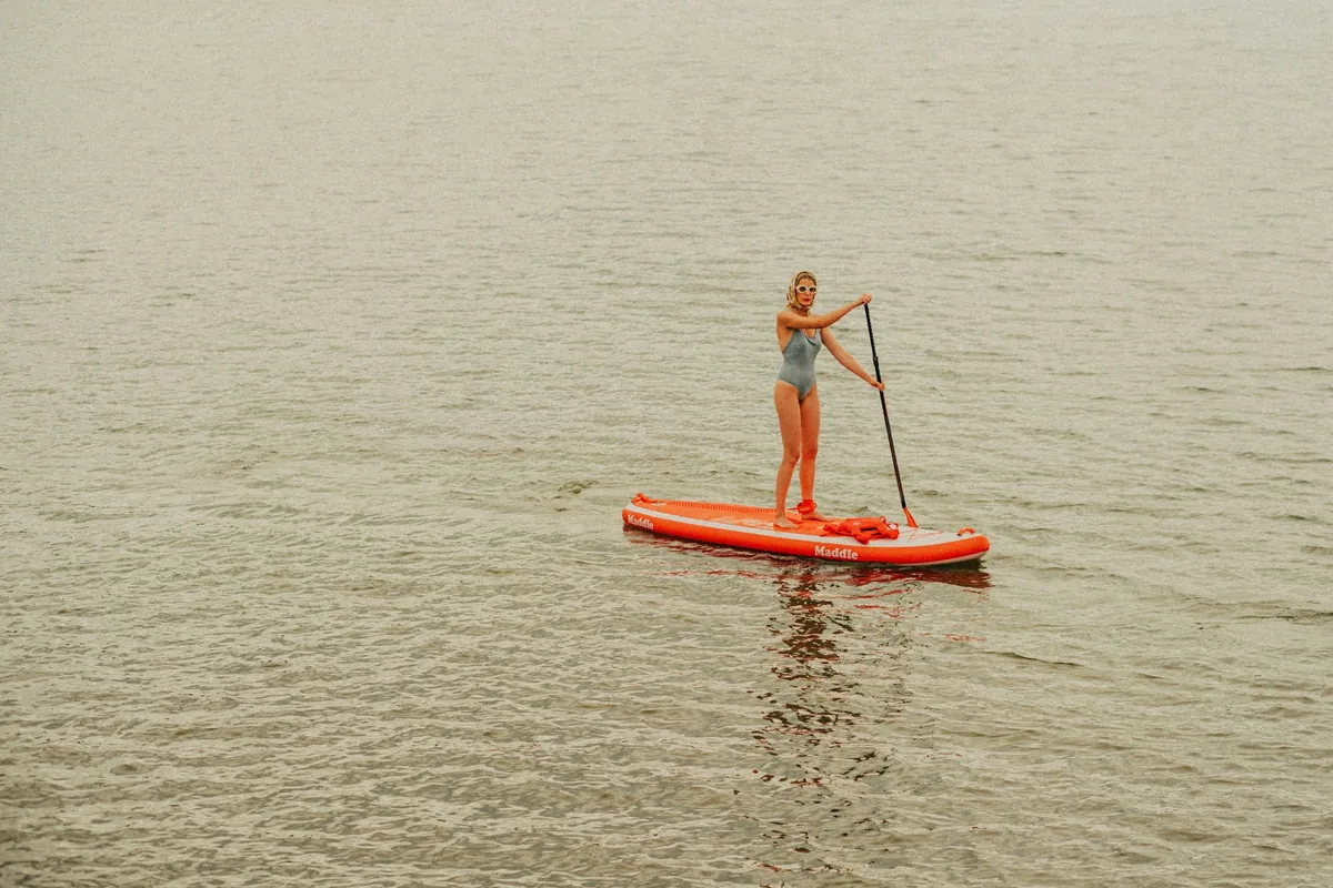 Pagayeur debout sur un paddle orange, vue aérienne sur une eau calme
