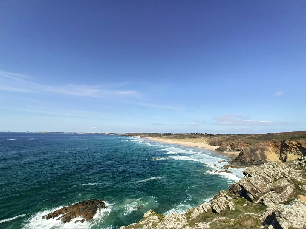 Vue depuis la falaise sur la plage de la Palue : des rochers au premier plan et des vagues qui déferlent vers une plage de sable