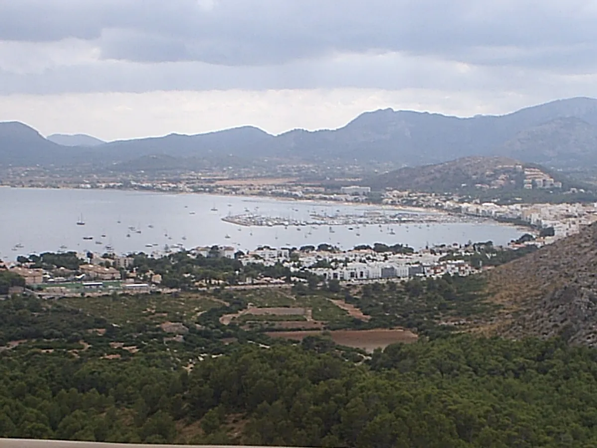 Vue en hauteur sur la Badia de Pollença, à Majorque, avec des bateaux au mouillage devant la ville et des montagnes en arrière-plan
