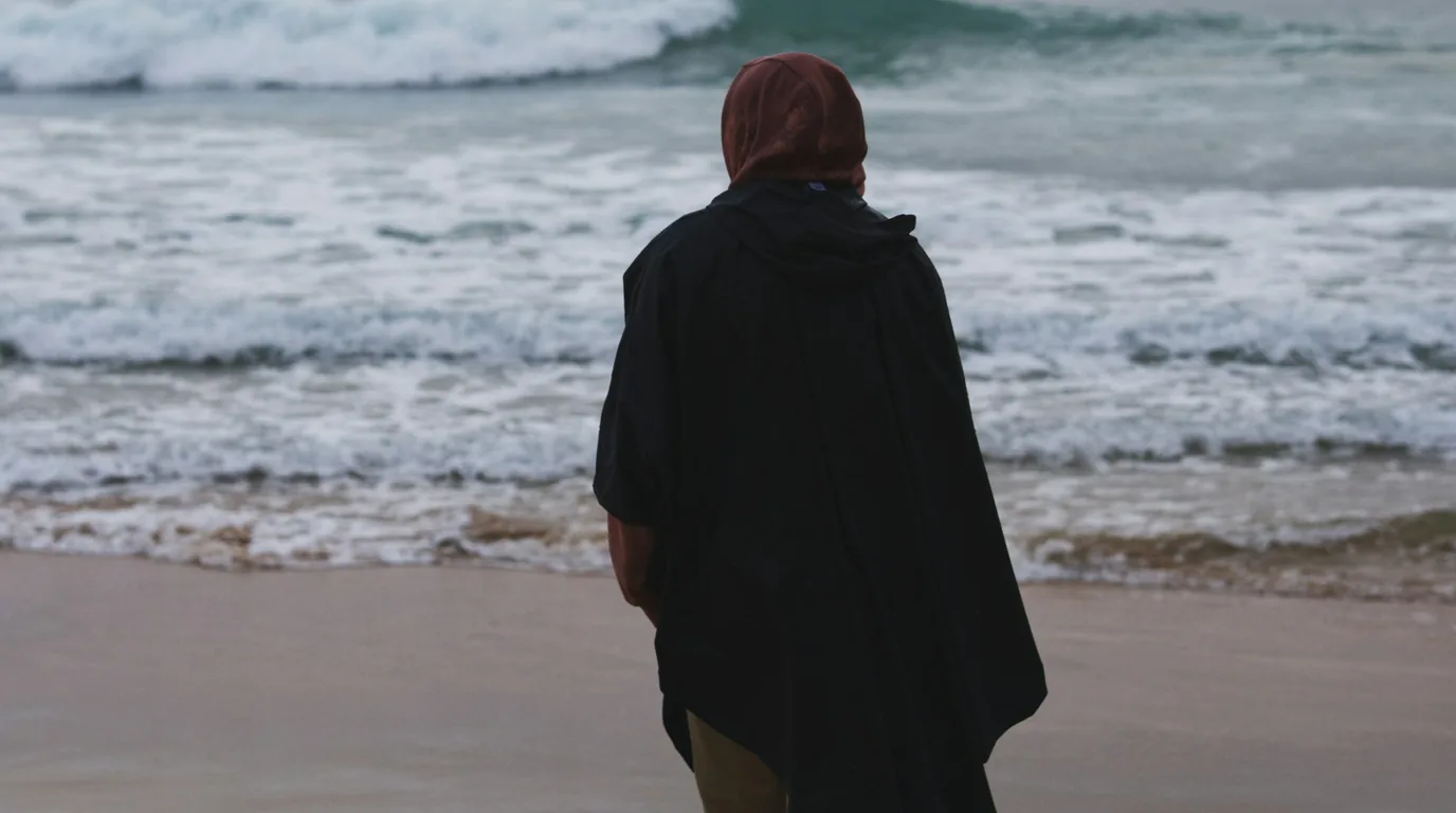 Surfeur avec un poncho de change face aux vagues sur une plage