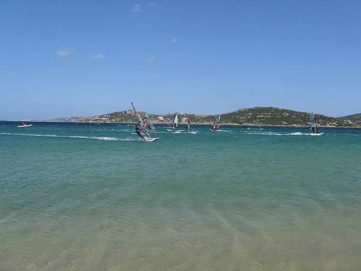 Véliplanchistes sur une eau turquoise à Porto Pollo, en Sardaigne, avec des collines au fond