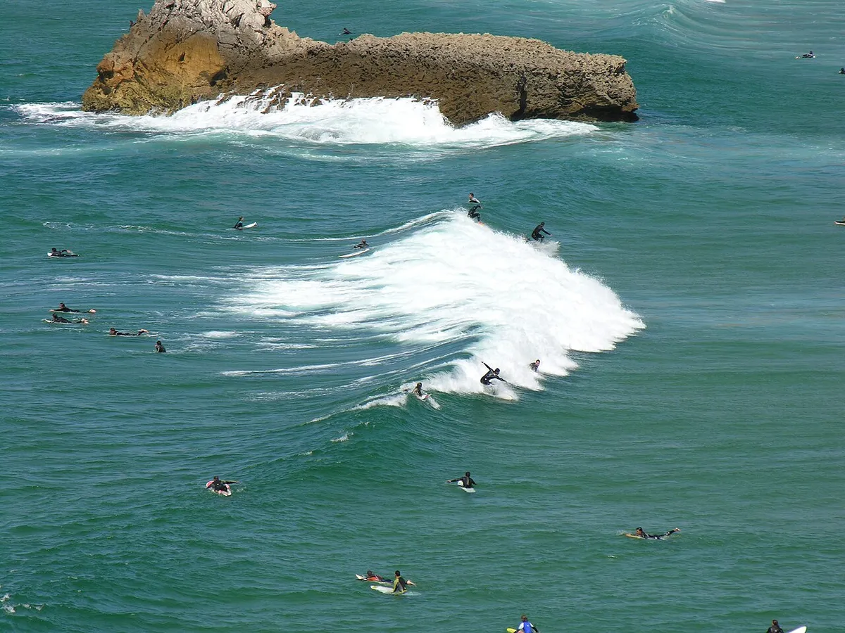 Surfeurs dans l'eau et sur une vague, à côté d'un rocher, à Sagres