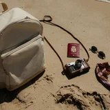 Passeport, appareil photo, lunettes de soleil et sac à dos posés sur le sable au bord de l'eau