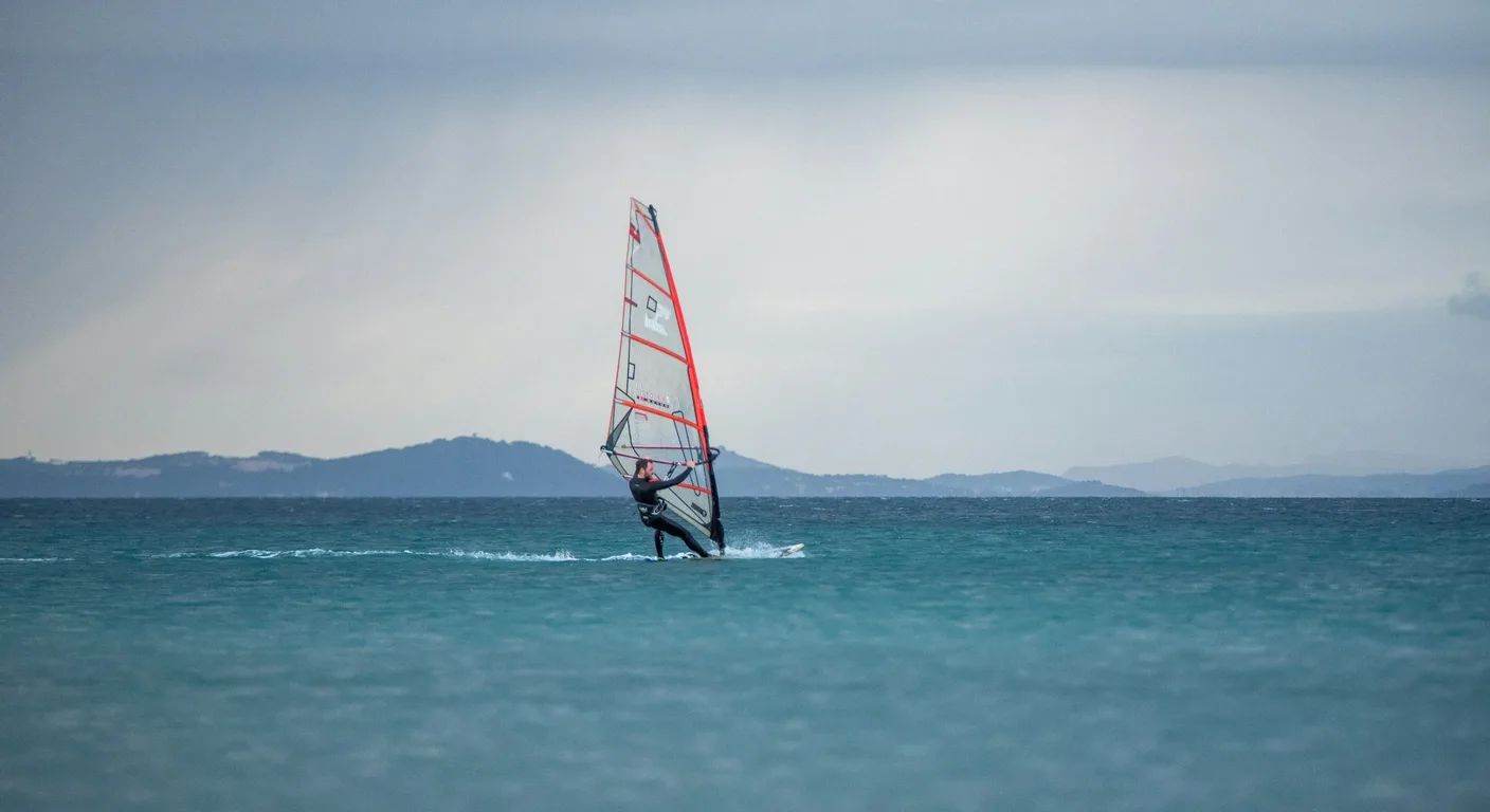 Windsurfeur sur une eau turquoise calme, des collines à l'horizon