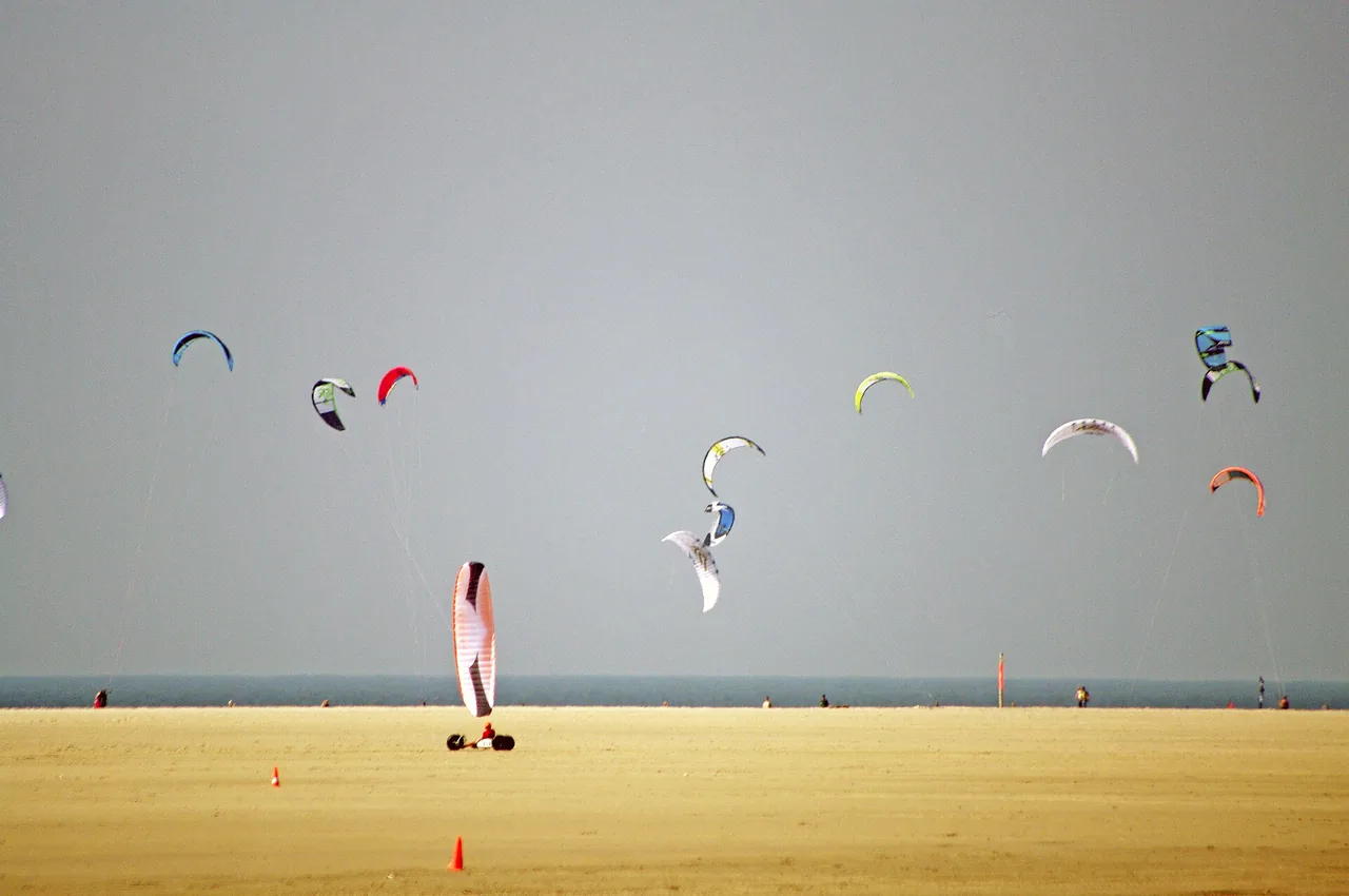 Un buggy tracté par une aile sur le sable de St. Peter-Ording, avec des ailes de kitesurf en arrière-plan