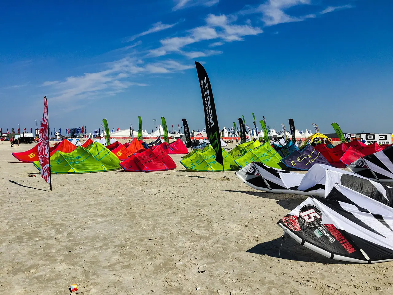 Rangées d'ailes de compétition posées sur le sable à la Coupe du monde de kitesurf de St. Peter-Ording, avec les tentes de l'événement derrière