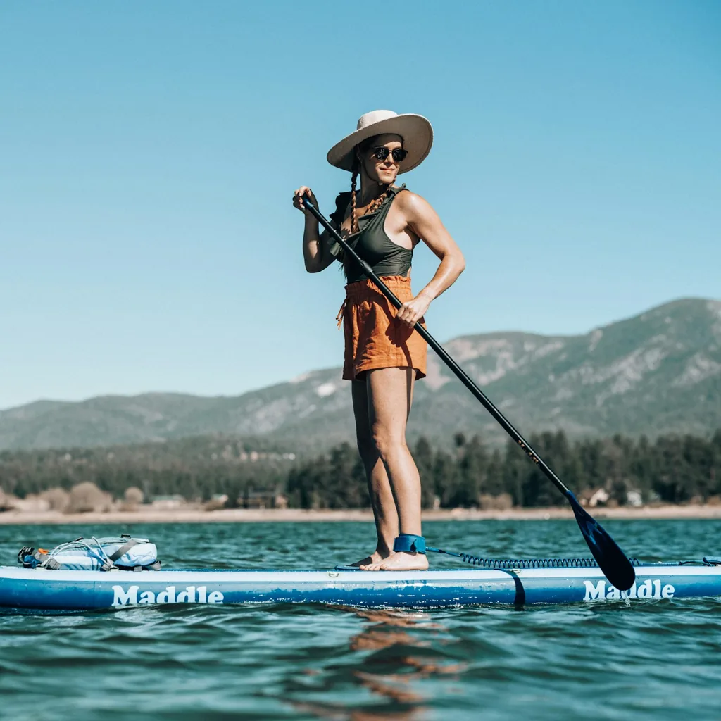 Une paddleuse debout sur un SUP gonflable, pagaie en main, leash à la cheville, devant des montagnes