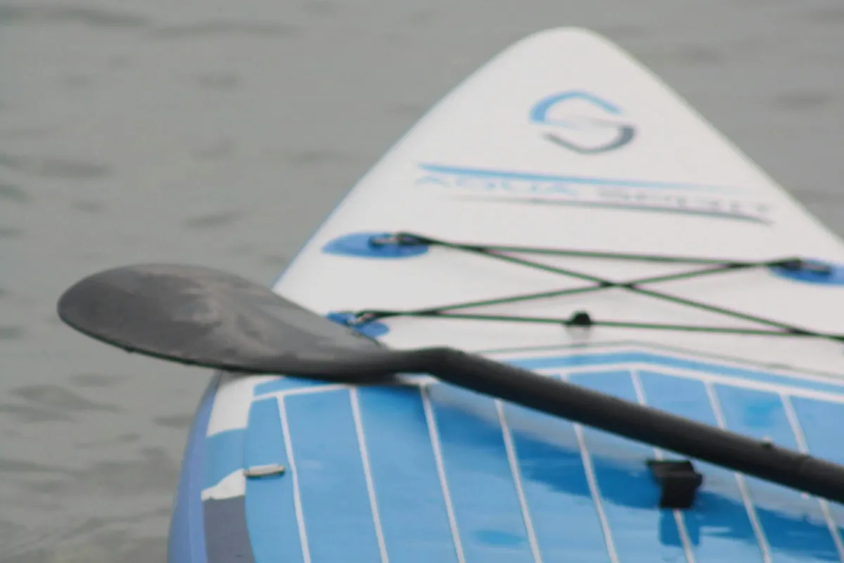 Gros plan sur l'avant d'une planche de SUP bleue et blanche, pagaie posée en travers