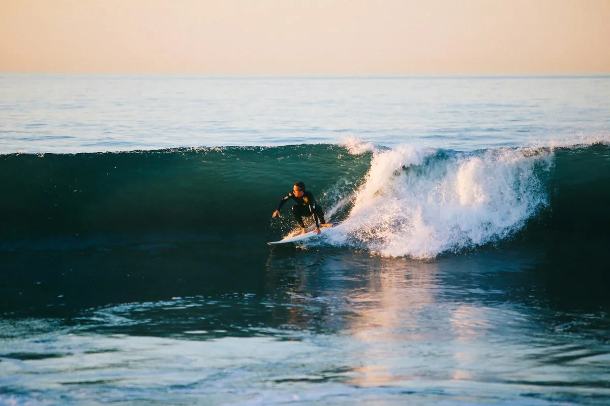 Surfeur en combinaison noire, accroupi sur sa planche, genoux fléchis, sur la face d'une vague