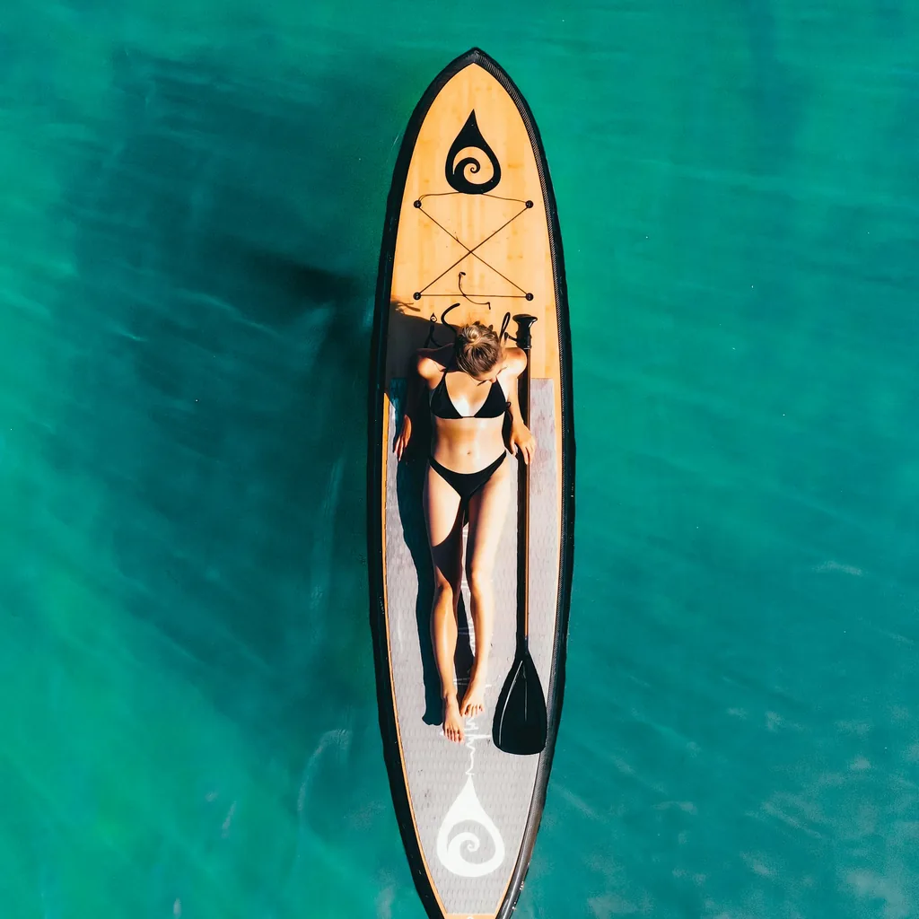 Vue aérienne d'une personne allongée sur une planche de SUP, pagaie posée à côté