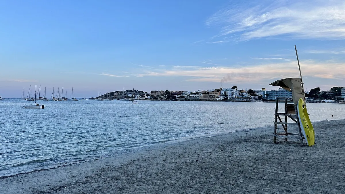 Baie calme de Talamanca, à Ibiza, avec un poste de secours sur le sable, des bateaux au mouillage et la ville sur la rive d'en face
