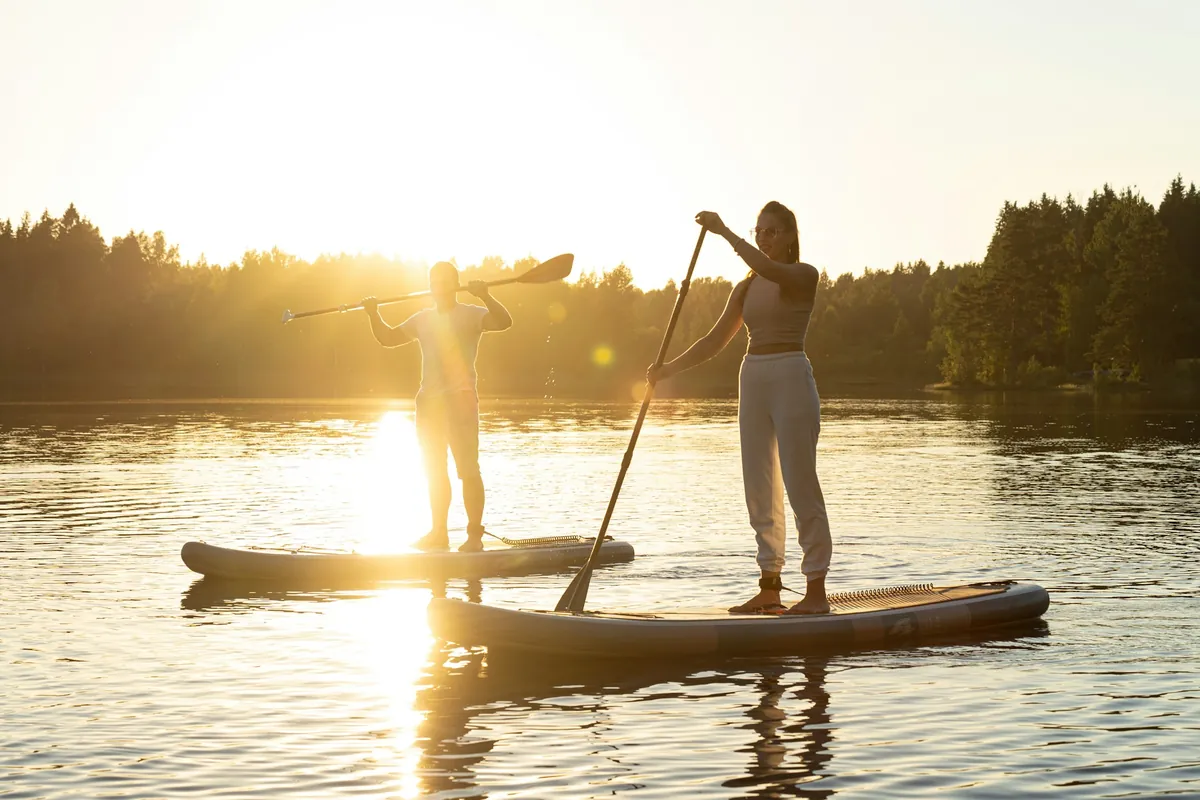 Deux paddleurs debout sur leurs planches de SUP, à contre-jour, sur une eau calme avec le soleil bas