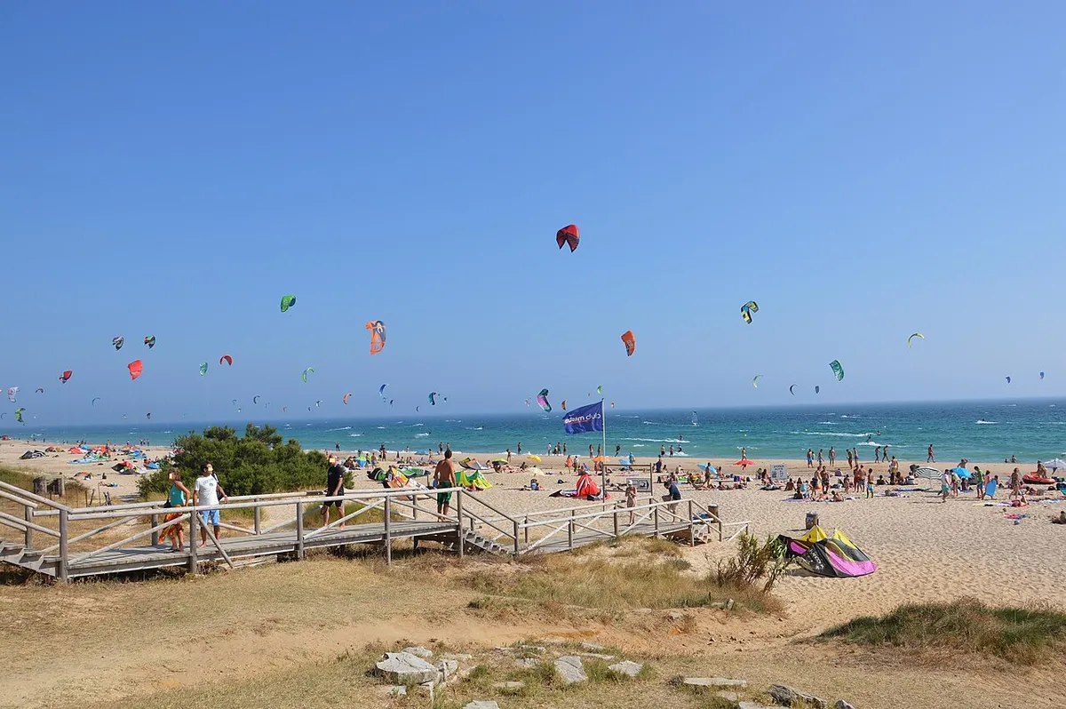 De nombreux kites dans le ciel au-dessus de la plage de Valdevaqueros, à Tarifa, avec du monde sur le sable