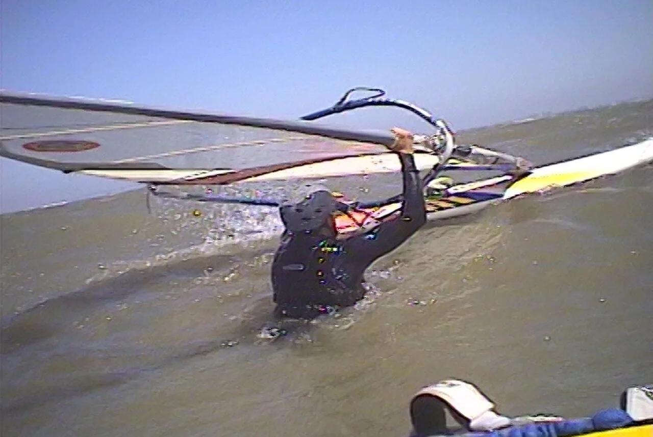 Un windsurfeur en plein waterstart, remontant sur sa planche en utilisant la puissance de la voile