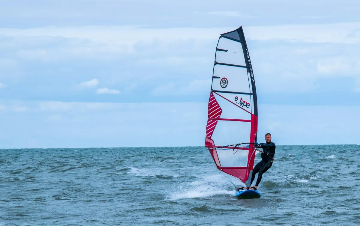 Windsurfeur en phase de planing sur une eau agitée, avec un sillage d'écume derrière la planche