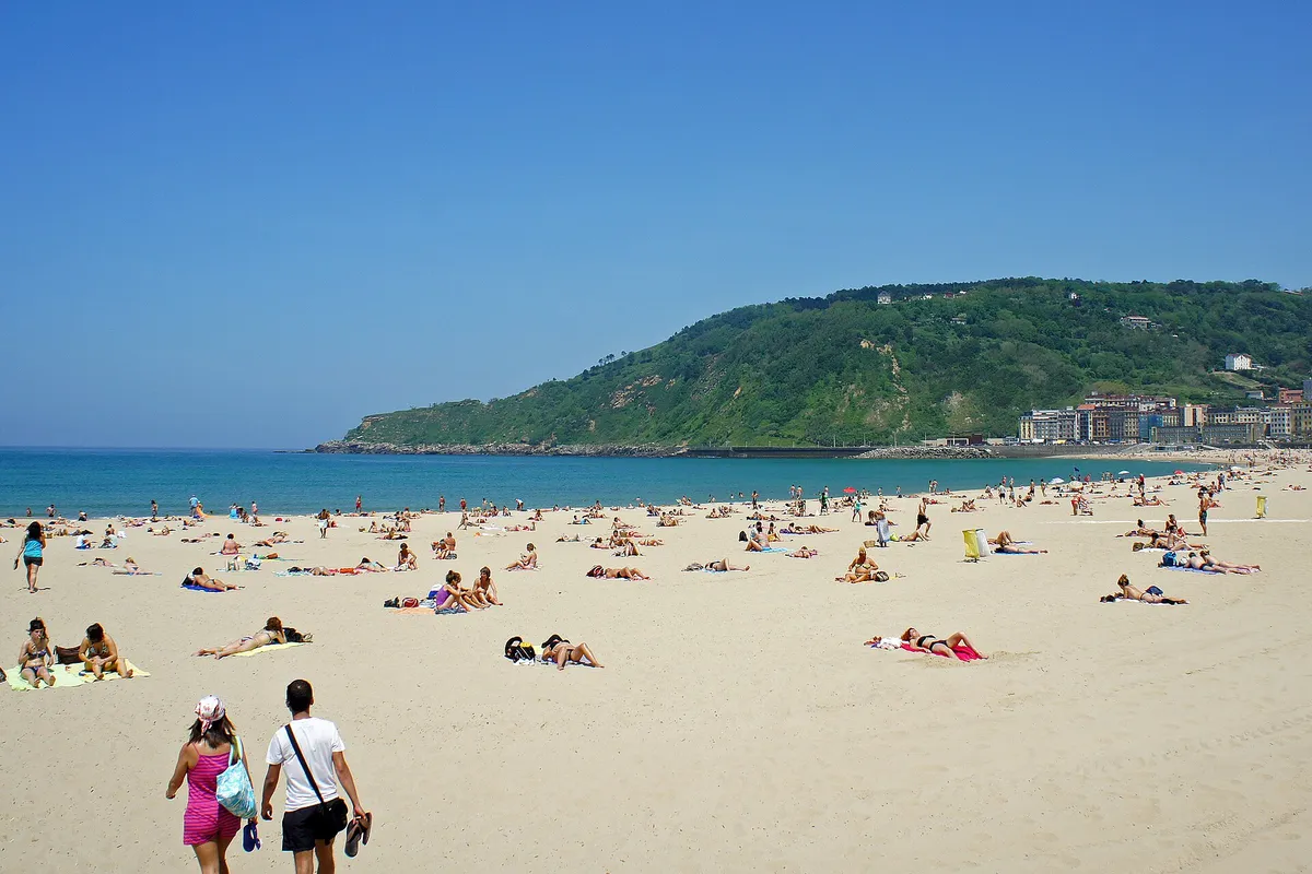 La plage de la Zurriola à Saint-Sébastien, avec des baigneurs sur le sable et une colline verte au fond